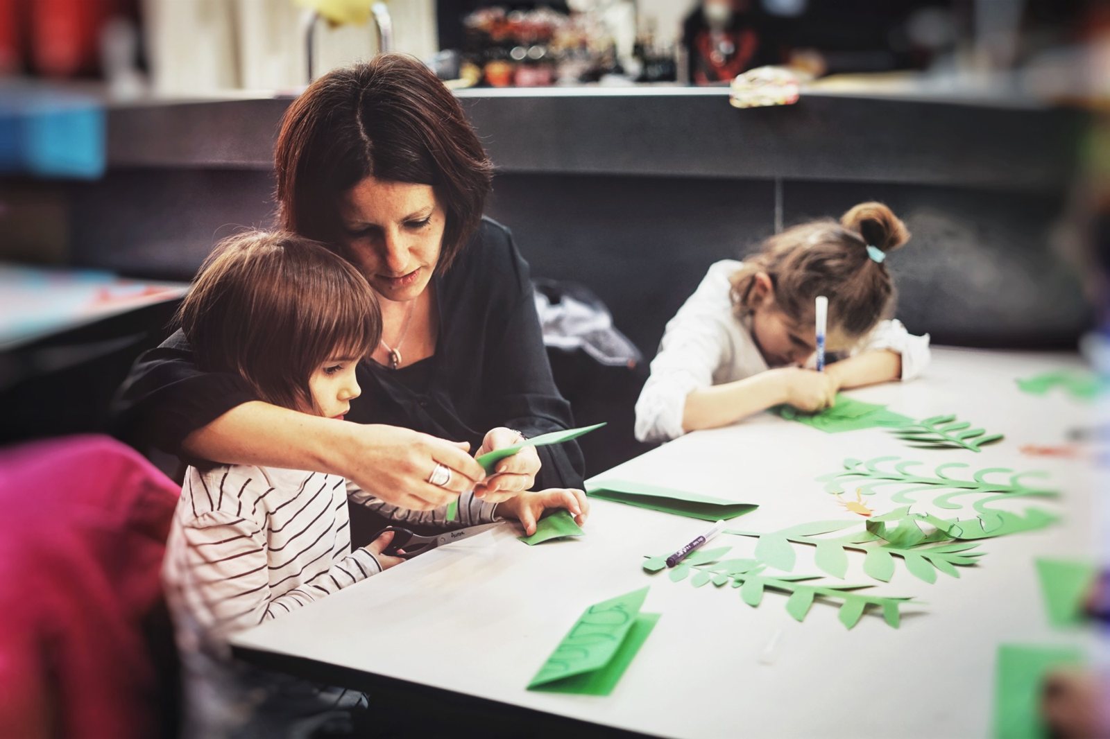 Atelier : une mère guide un enfant pour découper du papier vert